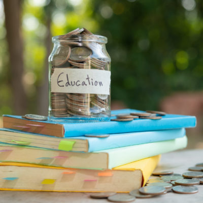 putting money coins saving in glass bottle for concept investment mutual fund finance and business, placed on the textbook. content money saving for education.